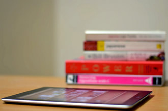 an electronic tablet sitting on a table top beside a stack of book