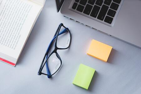 laptop and book on desktop alongside  glasses and post it notes 